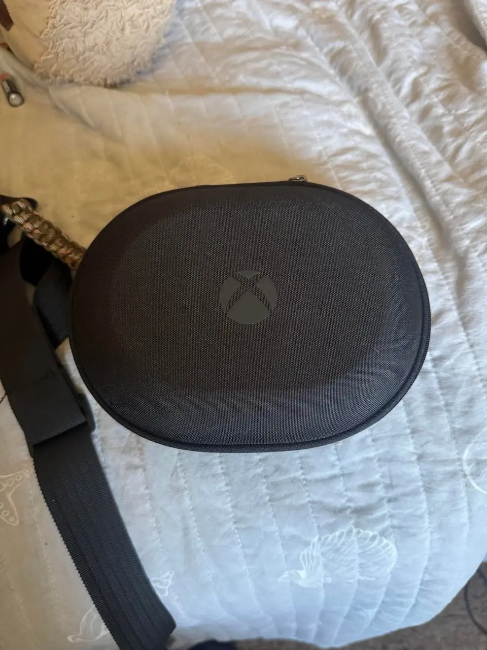 Чёрный жёсткий чехол с логотипом Xbox для беспроводных наушников лежит на кровати