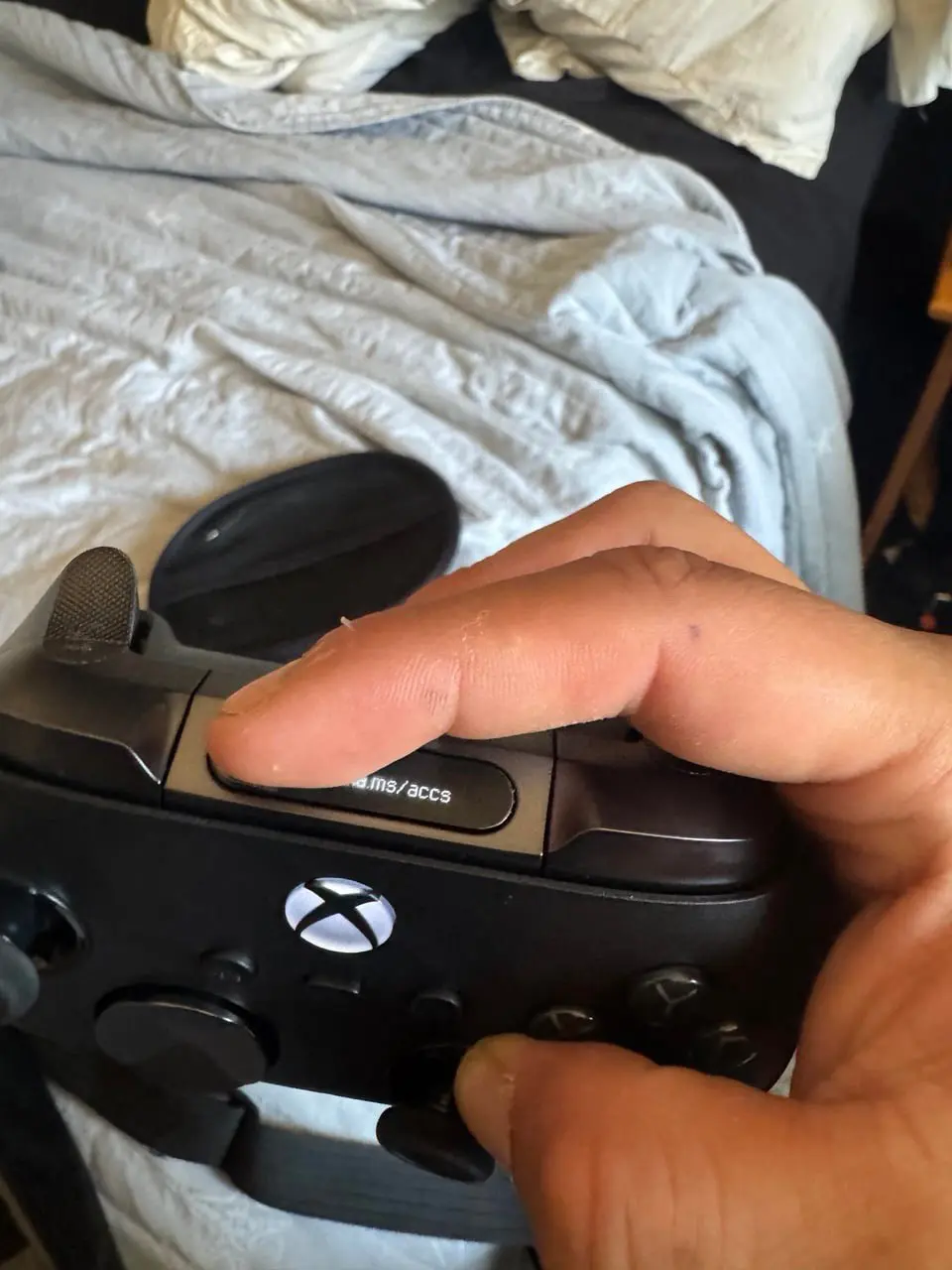 Рука держит геймпад Xbox и нажимает кнопку Share на фоне смятой постели