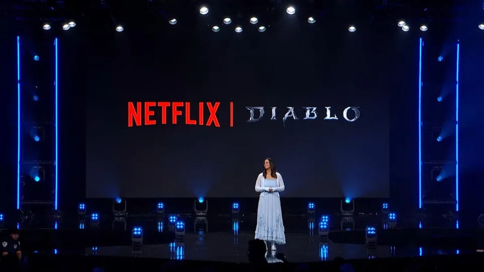 Презентация сериала Diablo на сцене Netflix с ведущей в белом платье на фоне синей подсветки